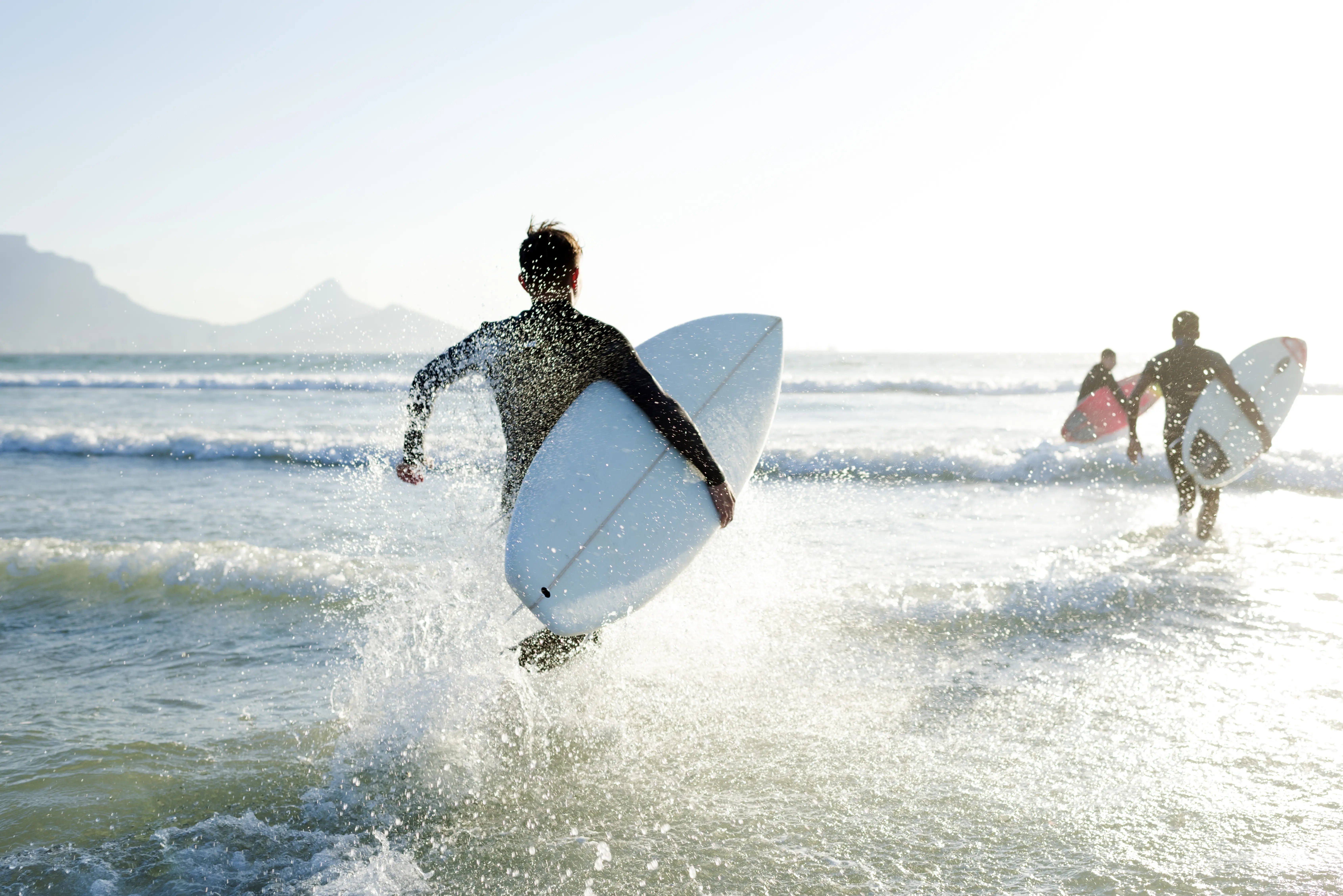 Boys Wearing Their Wetsuits Carrying Their Surfboards Run Into The Sea Gettyimages 525212990